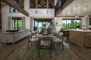 Un comedor amplio con techo alto y luz natural, que presenta una larga mesa con sillas y vistas al exterior.
