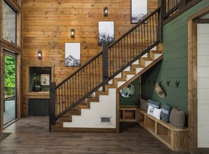 Un escalier en bois avec une rampe, un banc avec des coussins et des éléments de décoration fixés au mur, notamment des tableaux encadrés et des cornes d’animaux.