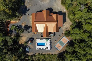An aerial view of a property with a swimming pool, tennis court, and a large building with a sloped roof.