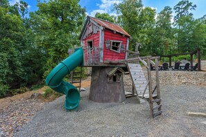 A playground with a red playhouse, a green slide, and a wooden climbing structure.