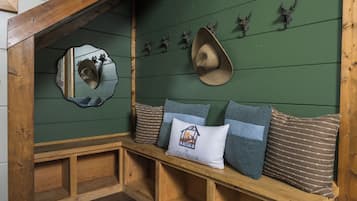 Un banco de madera con cojines, un espejo y cabezas de animales decorativas sobre una pared verde.