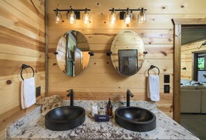 A wooden cabin interior with a bathroom vanity, two sinks, a mirror, and a towel rack.