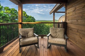 A wooden deck with two chairs facing a scenic view of trees and hills.
