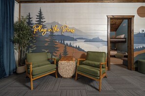 Una habitación con dos sillones verdes, una mesita redonda y un mural en la pared con una escena de bosque.