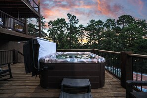 Un jacuzzi en una terraza de madera con vista a árboles y al atardecer.