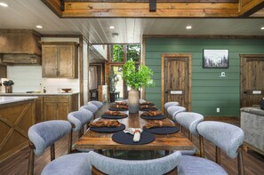 A dining area with a long wooden table, grey upholstered chairs, and a central vase with greenery.