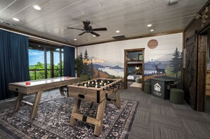 A room with a foosball table, a pool table, and a mural depicting a mountainous landscape.