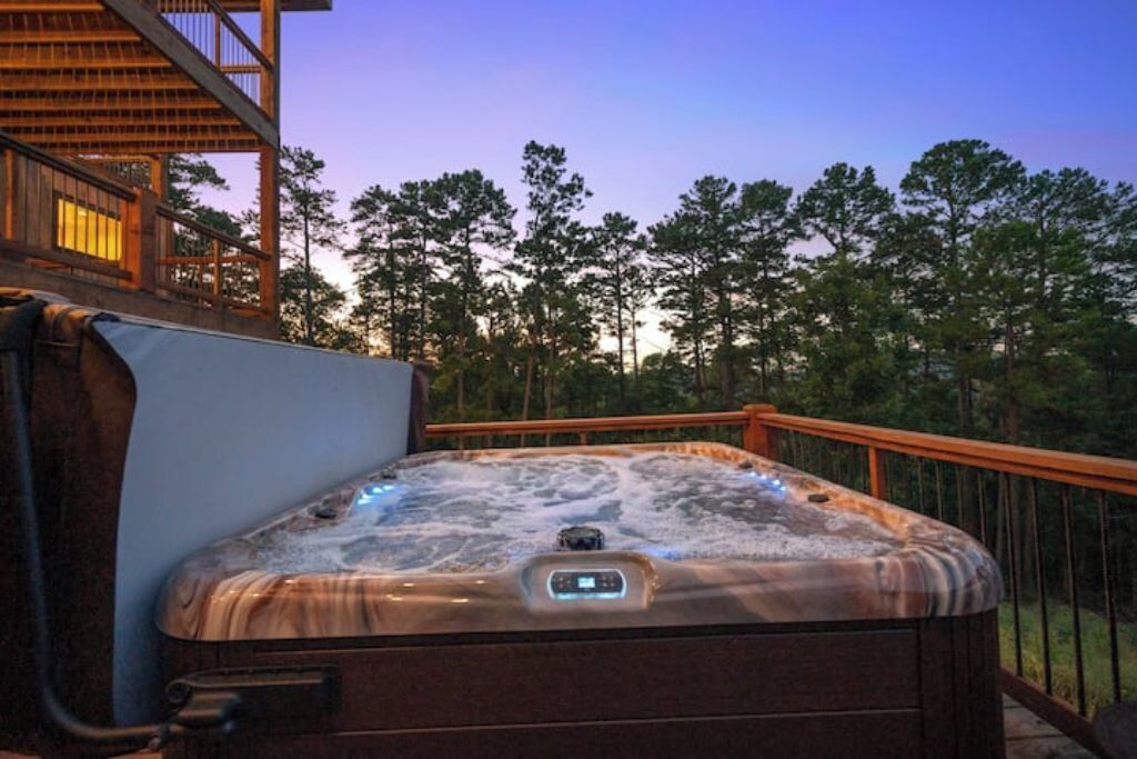 Ein Whirlpool auf einer Terrasse im Freien mit Holzgeländer, umgeben von Bäumen.