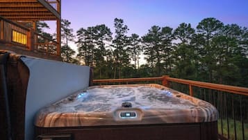 Ein Whirlpool auf einer Terrasse im Freien mit Holzgeländer, umgeben von Bäumen.