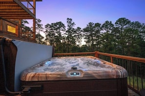 A hot tub on an outdoor deck with a wooden railing, surrounded by trees.