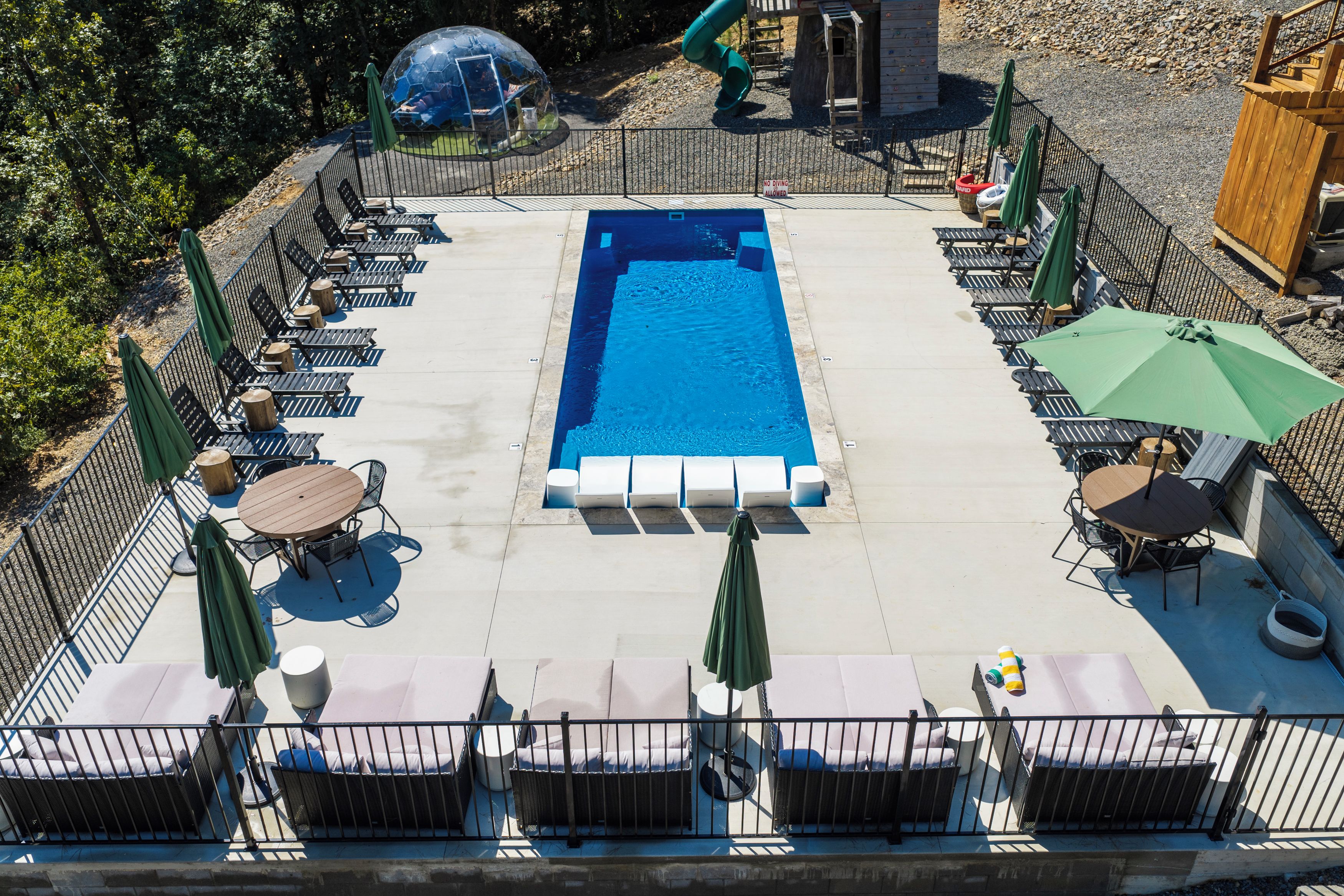 Ein rechteckiger Pool mit Liegestühlen und Sonnenschirmen, umzäunt.