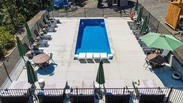 Ein rechteckiger Pool mit Liegestühlen und Sonnenschirmen, umzäunt.