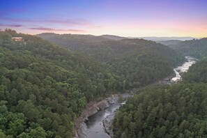 A river winding through a densely forested valley with a house on a hill overlooking the valley.