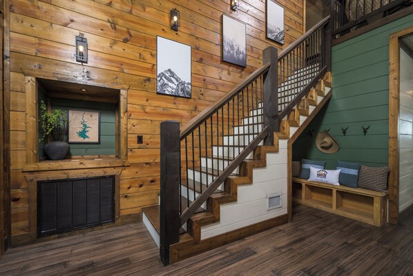 A wooden staircase with a metal railing, a green wall, and a bench with pillows.