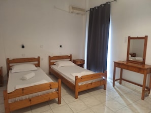Una habitación con dos camas de madera, una mesita pequeña de madera, un espejo y una cortina oscura.