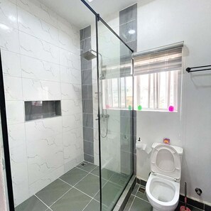 A modern bathroom with a glass shower enclosure, a toilet, and a window with colorful decorations. - Twin Heart Residence (Abuja)