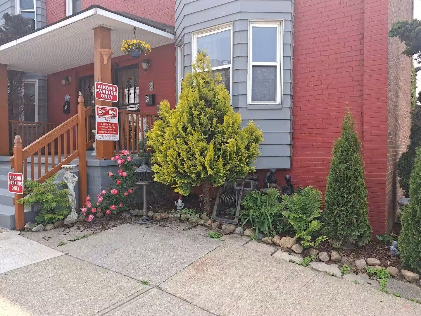 Une maison rouge avec un porche à l’avant, un escalier en bois et des panneaux indiquant les places de stationnement réservées aux clients d’Airbnb.