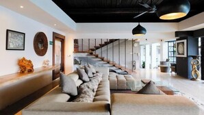 Un vaste espace de vie comprenant un long canapé, un escalier et des luminaires modernes.