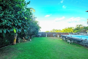 A backyard with a swimming pool, a grassy area, and a wooden deck. - The Lavana Villa Gajah Jimbaran (Bali)