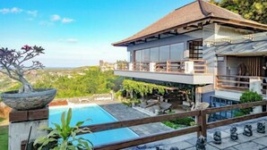 Une maison moderne à deux étages, dotée d’une piscine, de mobilier d’extérieur et offrant une vue sur le paysage environnant.