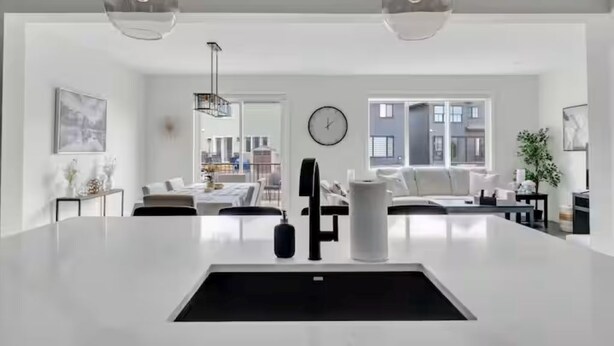Et moderne køkken med en central ø, hængende lamper og udsigt til opholdsstuen.