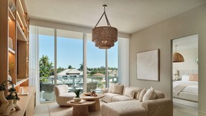 A modern living room with a large window, a woven coffee table, a beige sofa, and a hanging light fixture. - Spacious Balcony Retreat Close to Fort Lauderdale Beach – Recharge in Modern Ele (Fort Lauderdale)