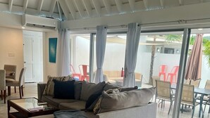 Ein modernes Wohnzimmer mit einem grauen Ecksofa, einem Glastisch und einem Essbereich mit roten Stühlen und einem Tisch.