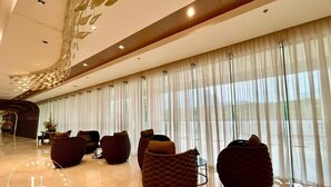 Un vestíbulo moderno con techo curvo, ventanas amplias con cortinas traslúcidas y varias zonas de estar con asientos acolchados.