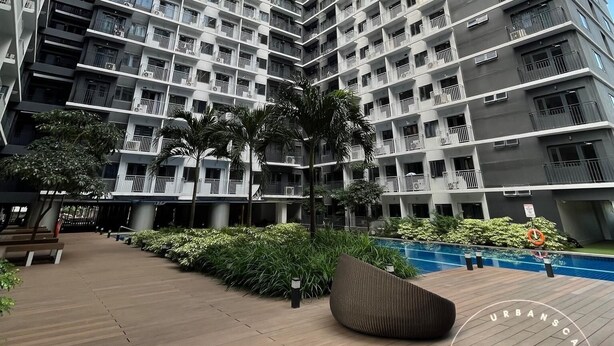 Un edificio residencial alto con varios balcones, una zona de piscina y vegetación circundante.
