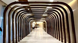 Un corredor moderno de hotel con un pasillo central flanqueado por columnas oscuras y curvas. Se observa un logotipo con el texto 