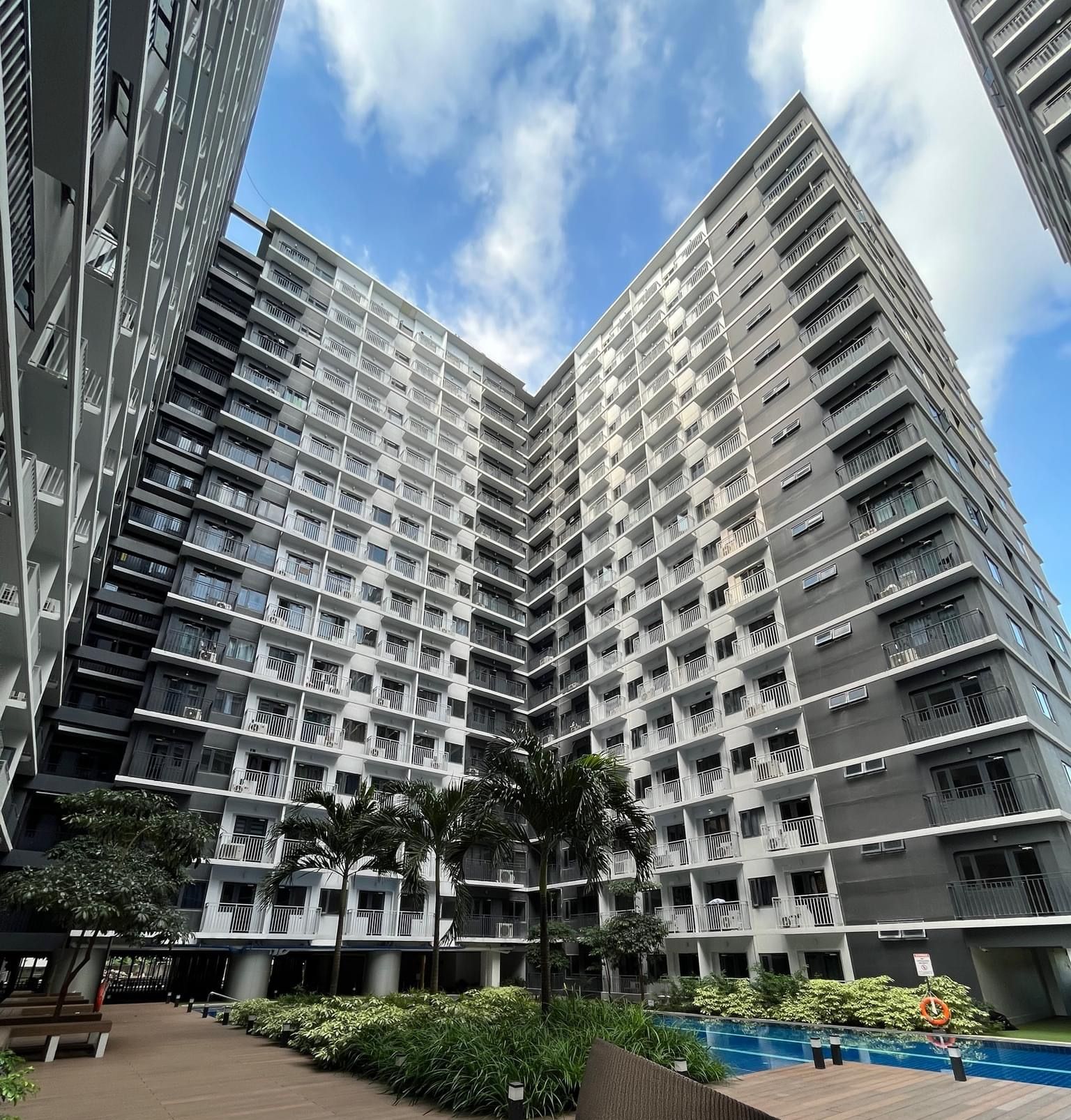 A high-rise residential building with multiple balconies, a pool area, and surrounding greenery.