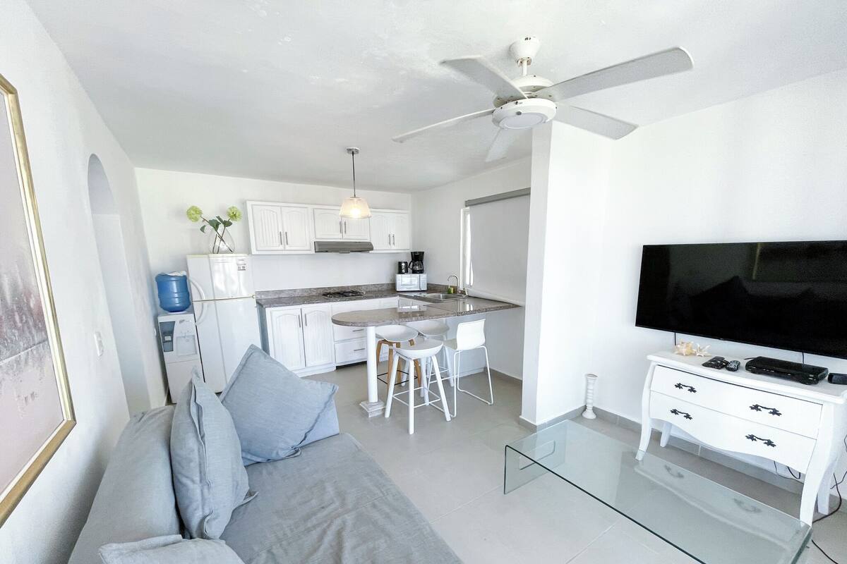 Un salon moderne avec une table basse en verre, un canapé avec des coussins, un téléviseur et un ventilateur de plafond.
