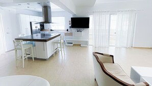 A modern kitchen with a central island, white cabinetry, and a flat-screen TV mounted above the island. - CASAS DEL MAR HOTEL Beach & SPA (Punta Cana)
