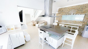 A modern kitchen with white cabinetry, a central island, and a stone accent wall. - CASAS DEL MAR HOTEL Beach & SPA (Punta Cana)