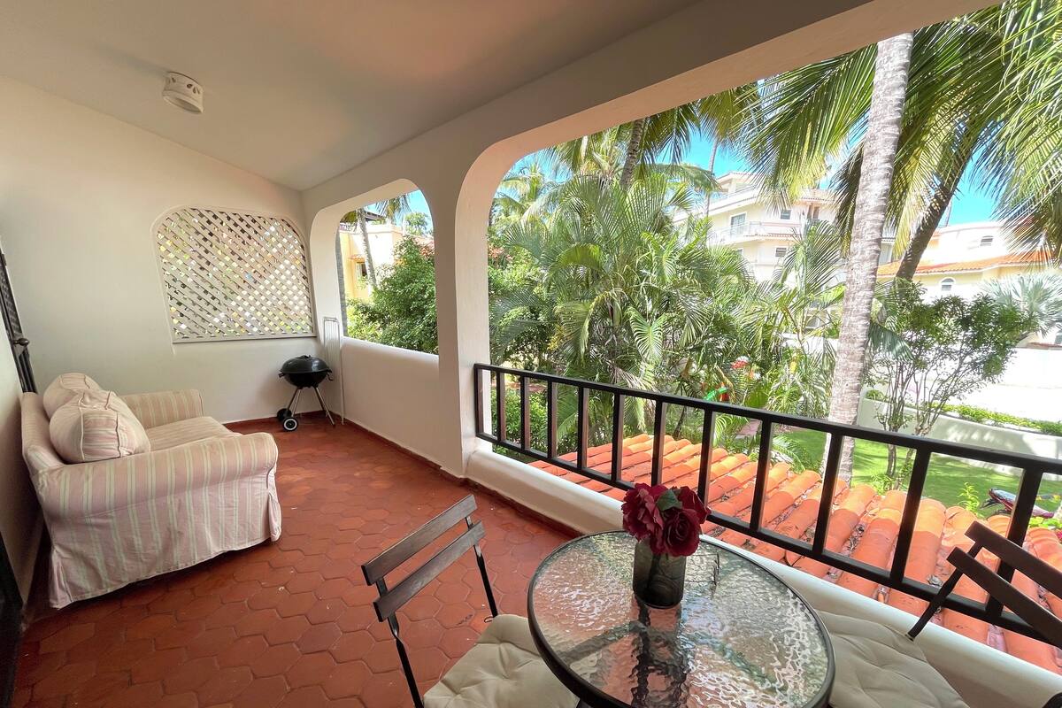 Un balcon avec un canapé, une table et des chaises, ainsi qu’un barbecue.