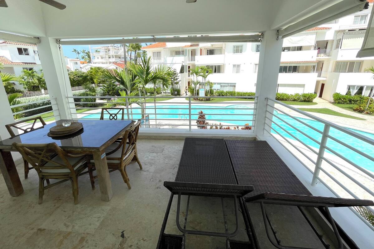 Un espace extérieur abrité comprenant une piscine, une table avec des chaises et un ventilateur de plafond.
