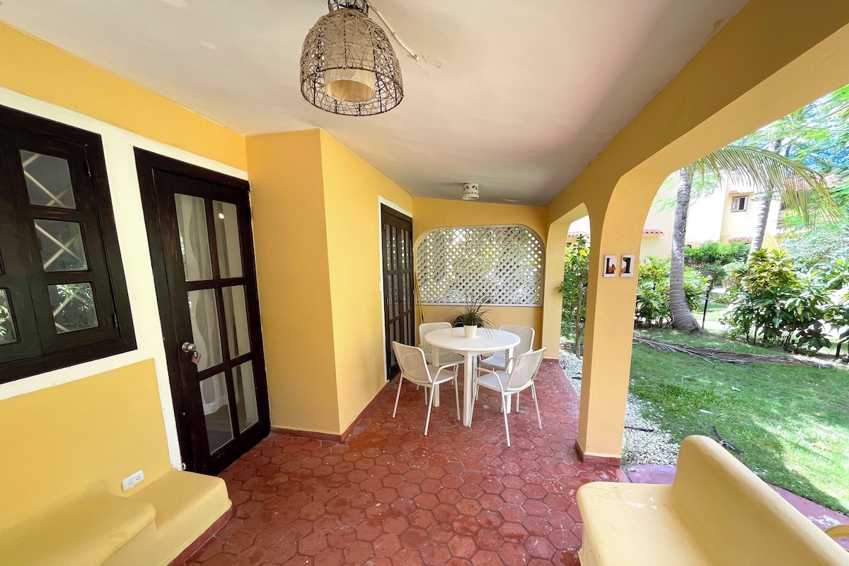 A covered patio area with a tiled floor, a round table with chairs, and a decorative ceiling light.