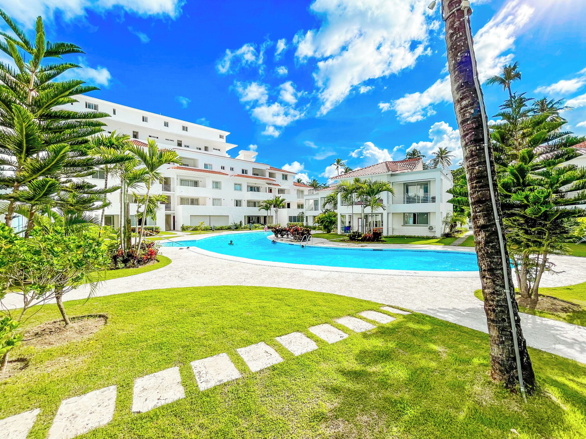 Un resort con piscina, palmeras y cielo azul despejado.