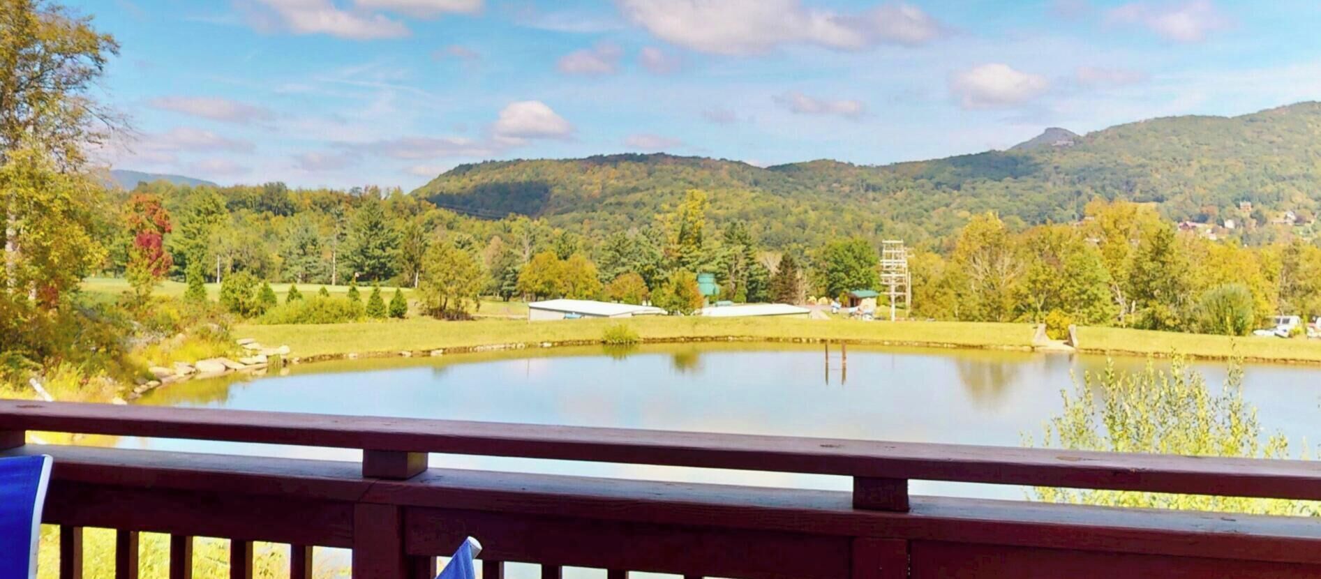 Vista panorâmica de um deck com vista para um lago, cercado por árvores e colinas.