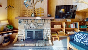 A cozy living room with a stone fireplace, wooden shelves, a television, and a blue sofa.