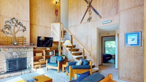 A spacious living room with a stone fireplace, wooden furniture, a television, and a staircase leading to another room.