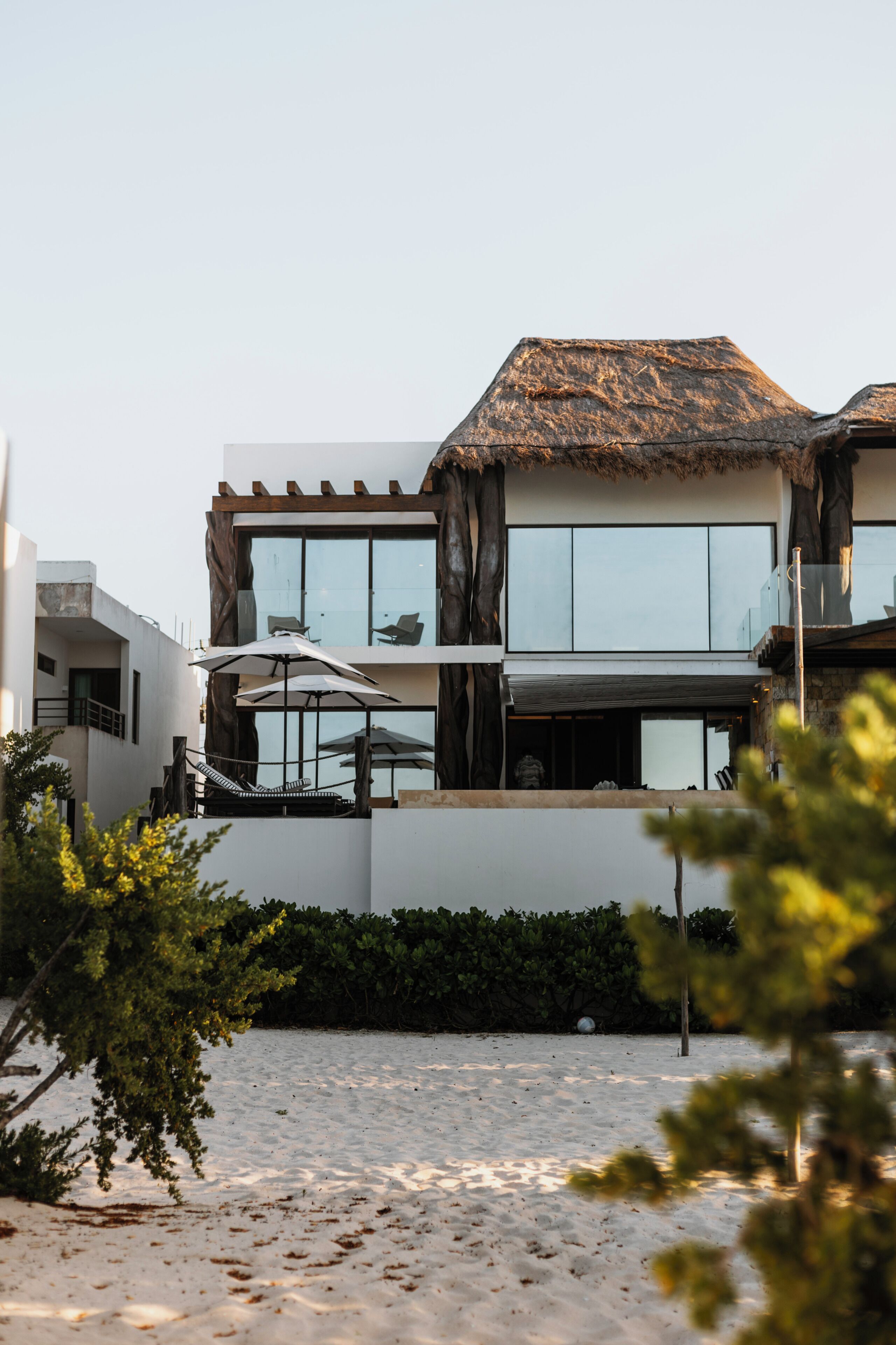 A modern two-story building with large windows, a thatched roof, and outdoor seating.
