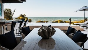 Un espace repas extérieur avec vue sur l’océan, comprenant une grande coupe décorative posée sur la table, des chaises et un parasol.