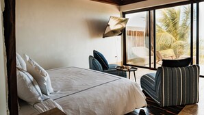 Une chambre à coucher comprenant un lit, une chaise, une petite table et une grande fenêtre donnant sur des palmiers.