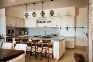 A kitchen with white cabinets, a central island with stools, a stainless steel oven, and a hanging light fixture. - Beach House Costa Yucatan by Trobbu Collection (Dzemul)