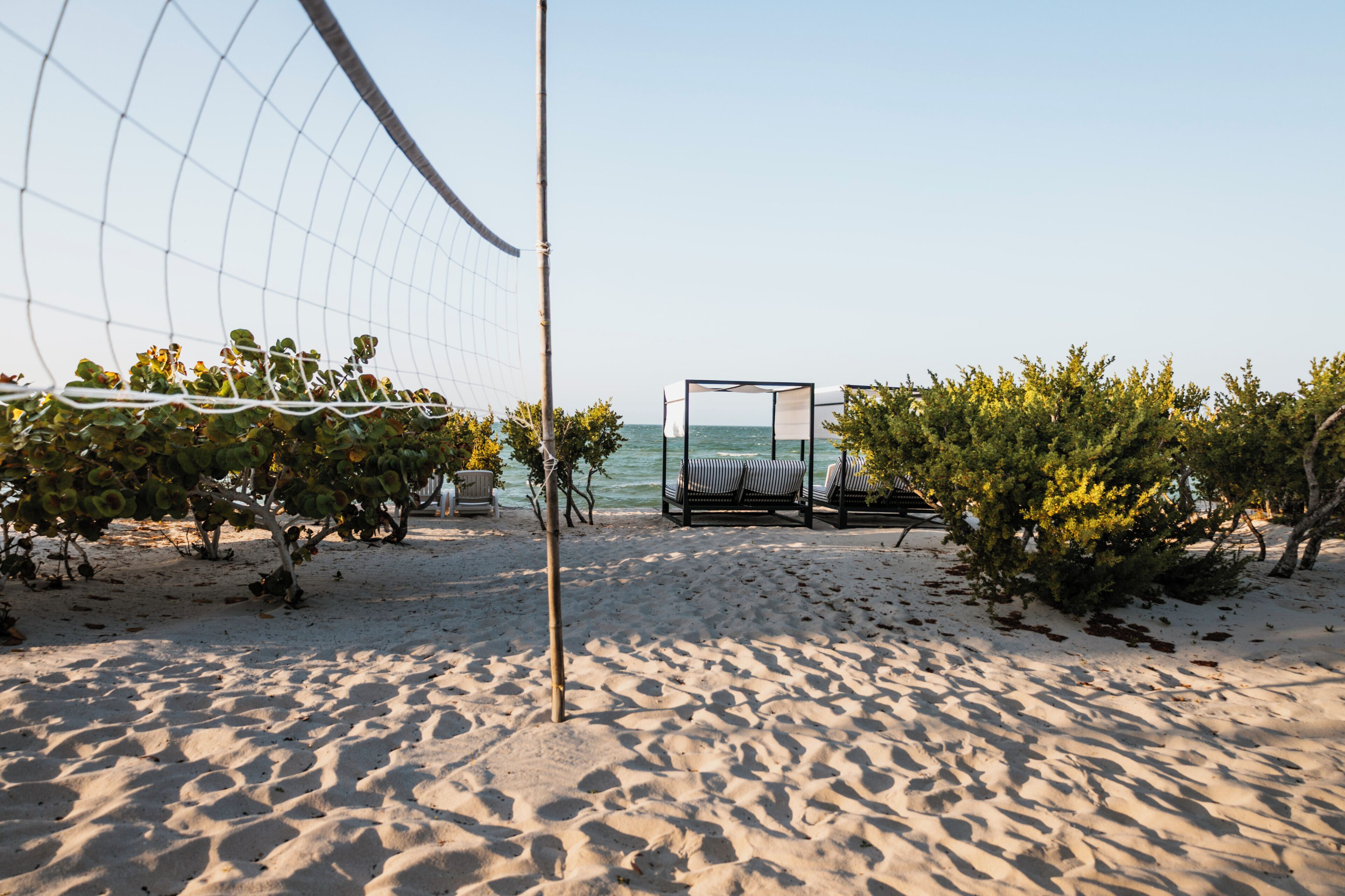 En strand med volleyballnet, liggestole og havudsigt.