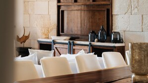 Un comedor con una mesa de madera y sillas blancas, una pared de piedra y un aparador de madera con objetos decorativos.