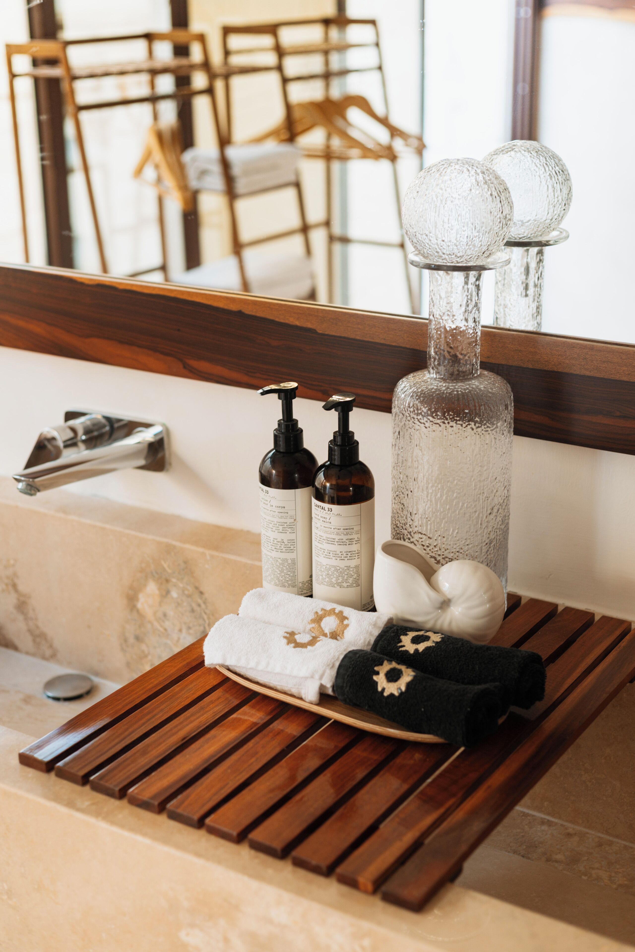 A bathroom vanity with a wooden tray holding toiletries, a large mirror, and a towel rack in the background.
