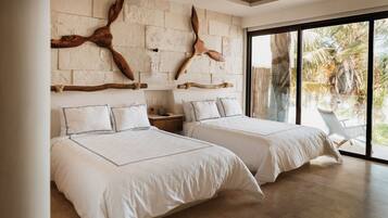 A modern bedroom with two beds, a stone wall, and a large window.