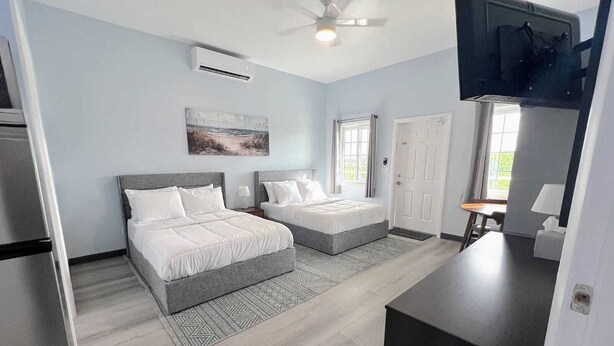 A modern bedroom with two beds, a ceiling fan, an air conditioning unit, and a television. - Town Center Abaco (Marsh Harbour)